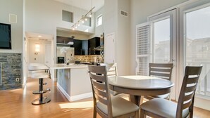 Una cocina moderna con una isla central, un comedor con una mesa redonda y sillas, y un ventanal con persianas.