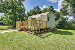 Ein kleines, eingeschossiges Holzhaus mit Veranda und überdachtem Bereich, umgeben von Gras und Bäumen.