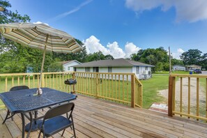 A wooden deck with a table and chairs, an umbrella, and a house in the background. - Peaceful Gulf Coast Getaway: 3 Mi to Boat Ramp! (West Orange)
