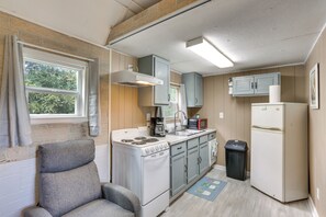 A compact kitchen with a stove, sink, and refrigerator, wooden walls, and a window with curtains. - Peaceful Gulf Coast Getaway: 3 Mi to Boat Ramp! (West Orange)