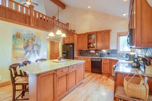 A spacious kitchen with wooden cabinets, a large island, and a dining area with chairs. - Colorado Riverfront Escape! Fish, Hike & Relax (Pine)