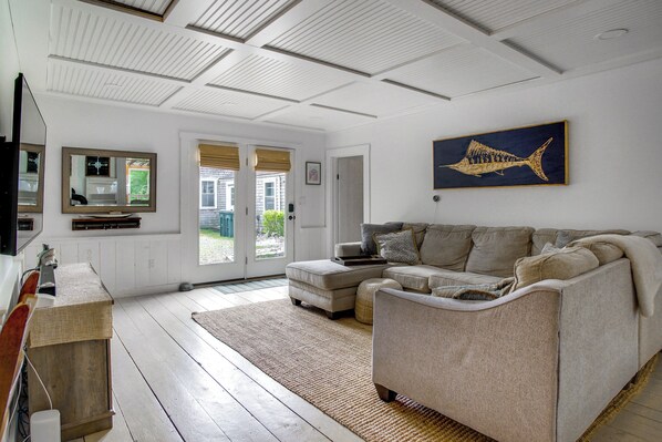 Una sala de estar con un sofá modular, un televisor de pantalla plana, un cuadro grande de peces y piso de madera.