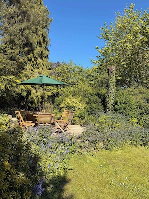 An outdoor seating area with a table and chairs, surrounded by lush greenery and flowering plants. - Garden Cottage on the edge of Oxford (Kennington)