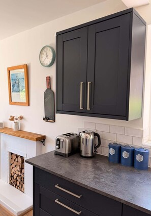 Cucina con mobili scuri, una sveglia, una foto incorniciata, una bottiglia, un tostapane, un bollitore e contenitori portaoggetti.