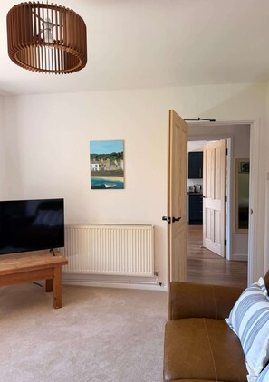 Un soggiorno con televisione, una panca in legno, un divano in pelle marrone, una porta in legno e un quadro appeso al muro.