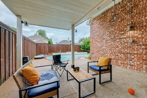 Un patio techado con mobiliario exterior, una pared de ladrillo y una piscina.