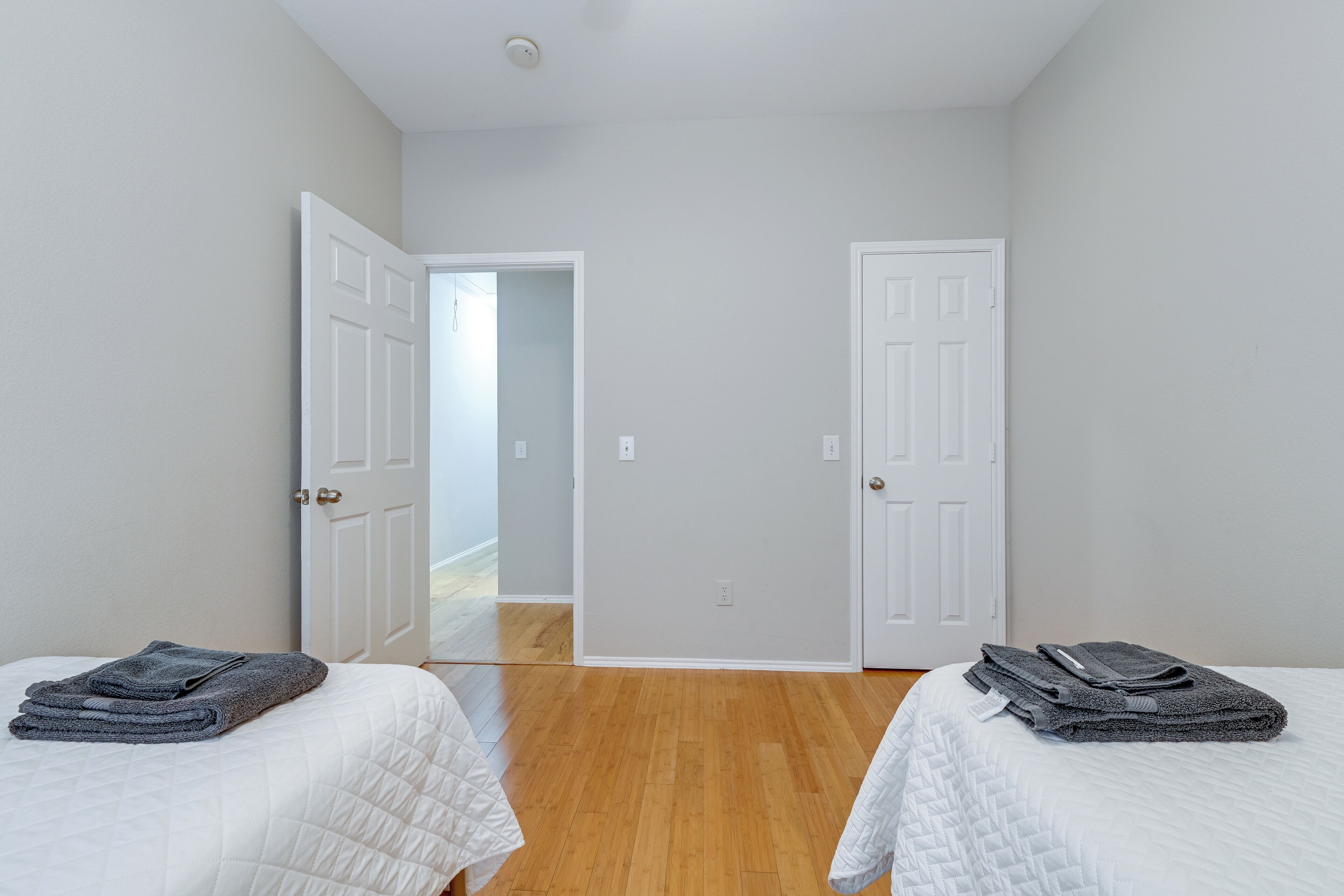 A room with two beds, white walls, wooden flooring, and white doors.