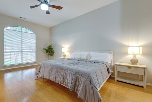 Un dormitorio con cama, lámparas de noche, mesita de noche, ventilador de techo y un amplio ventanal con persianas.