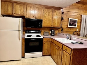 A kitchen with wooden cabinets, a white refrigerator, a black stove, a microwave, a toaster, and a coffee maker. - Real Private Cabin with Idyllic for a Secluded Romantic Getaway in Arkansas (Eureka Springs)