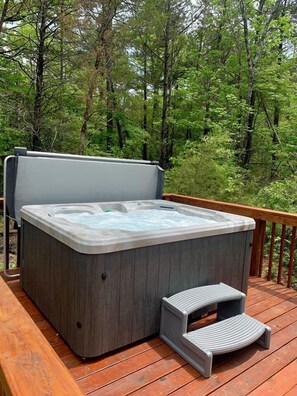 Ein Whirlpool auf einer Holzdielen-Terrasse mit einer Stufe, umgeben von bewaldeter Landschaft.