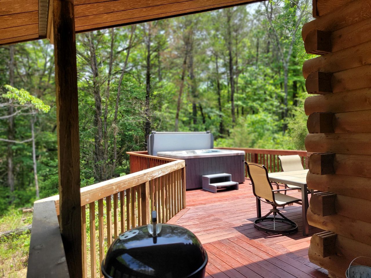 Une terrasse en bois avec un jacuzzi, une table et des chaises, le tout entouré d’une forêt.