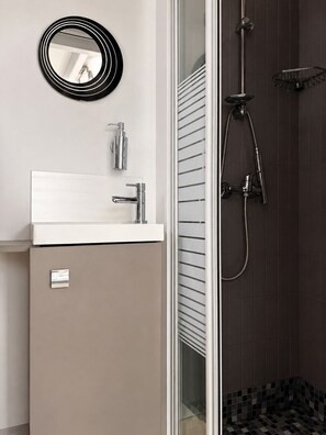 A bathroom with a white sink, a mirror, and a shower with a dark tiled wall. - Cozy Cottage with Veranda in Les Sables d'Olonne (Les Sables-d´Olonne)