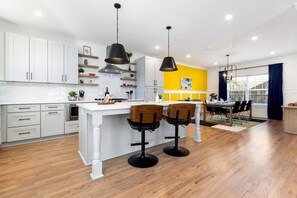 A modern kitchen with white cabinetry, a central island, bar stools, pendant lighting, and a dining area with a table and chairs. - Luminous Urban Vacation Rental Haven near Catawba River in North Carolina (Charlotte)