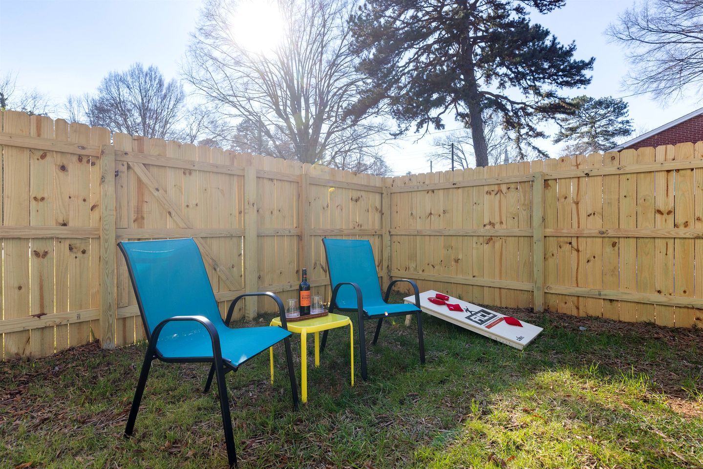Un jardin avec une clôture en bois, deux chaises bleues, une petite table et une bouteille de vin.