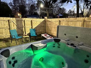 Un jacuzzi con chorros, rodeado por una valla de madera, con sillas y una mesa al fondo.