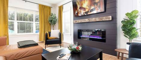 Ein modernes Wohnzimmer mit Kamin, einer Couch, einem Couchtisch und einem an der Wand befestigten Fernseher.