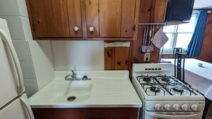 Een compacte keuken met houten kastjes, een witte spoelbak, een fornuis en een koelkast.