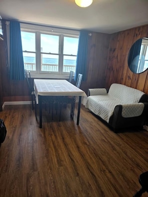 A room with a wooden floor, a dining table with chairs, a sofa, and a large window with a view of the sea. - Drift Away in a Peaceful Oceanfront Escape in North Truro, Massachusetts (North Truro)