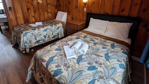 Een kamer met twee bedden, houten wanden, een plafondlamp en een kleine tafel.
