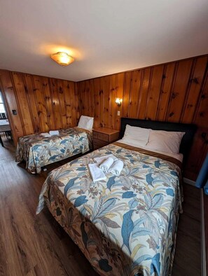 A room with two beds, wooden walls, a ceiling light, and a small table. - Drift Away in a Peaceful Oceanfront Escape in North Truro, Massachusetts (North Truro)