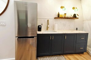 Une cuisine moderne dotée d’un réfrigérateur en acier inoxydable, de meubles sombres, d’un plan de travail en marbre, d’un robinet doré et d’une étagère où sont rangés des ustensiles de cuisine.