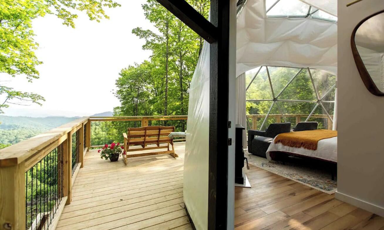 A room with a wooden deck, a bench, and a bed with a view of the outdoors.