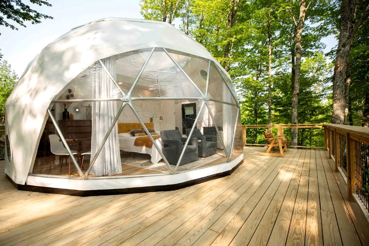 A geodesic dome structure with a wooden deck, a bed, a desk, and a chair inside.