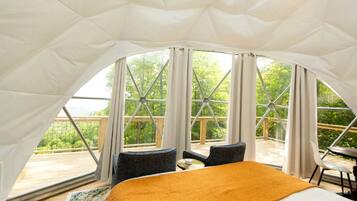 A tented accommodation with a bed, two chairs, and a table.