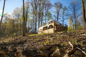 Une cabane en bois avec un toit en pente, de grandes fenêtres et des fondations en pierre, située dans une zone boisée.