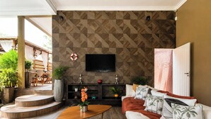 Un salón con pared estampada, un televisor de pantalla plana, un sofá con almohadas de palmera, una mesa de centro y una escalera que lleva a un espacio exterior.