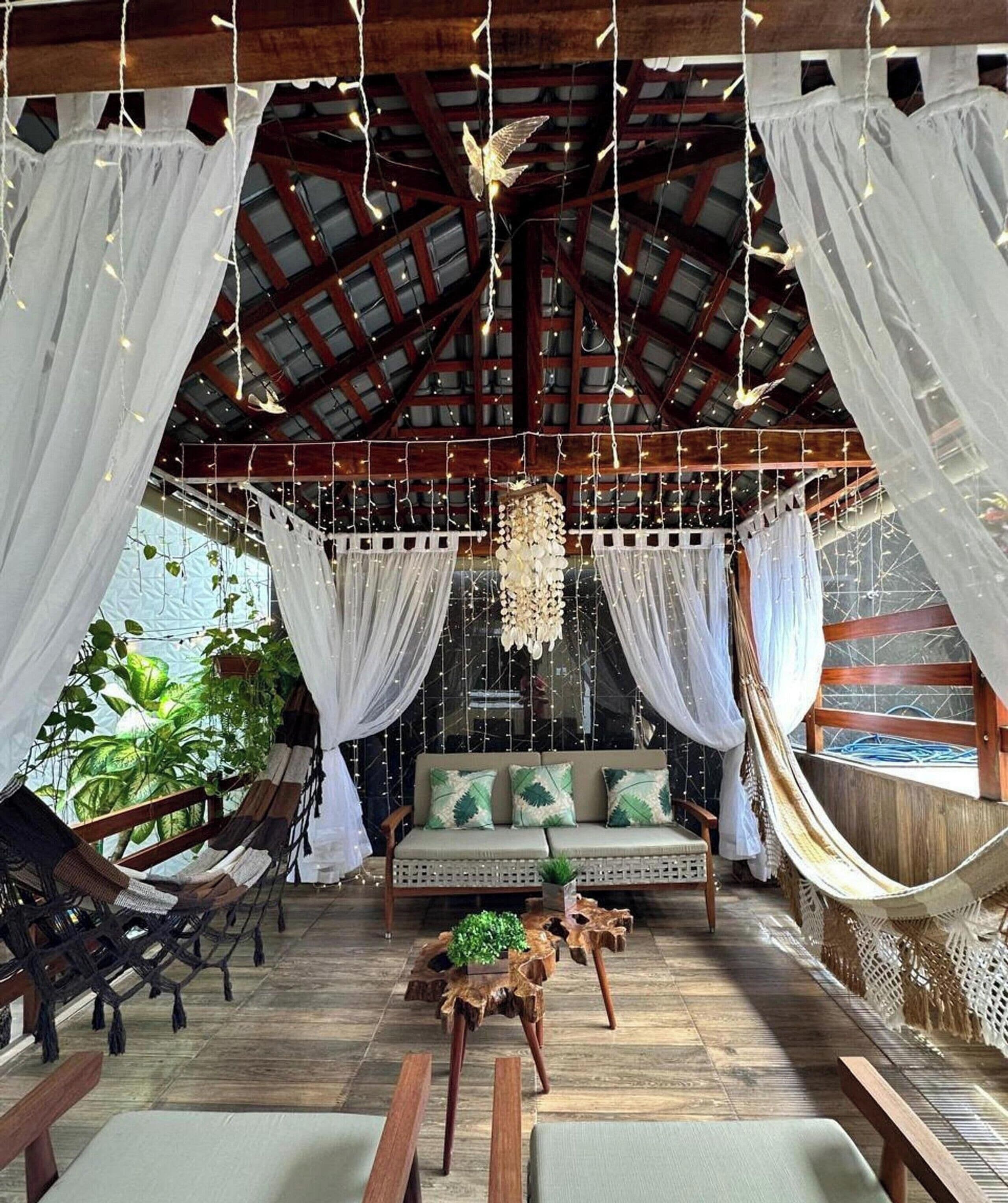 A cozy, rustic room with a hammock, a cushioned seating area, and a hanging light fixture.