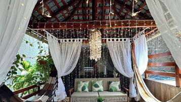A cozy, rustic room with a hammock, a cushioned seating area, and a hanging light fixture.