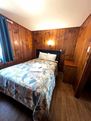 A wooden-paneled room with a bed, a nightstand, and a wall-mounted light fixture. - Recharge by the Ocean in Total Tranquility in North Truro, Massachusetts (North Truro)