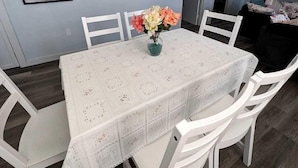 A dining area with a table set for four, white chairs, and a vase with flowers. - Cozy Coastal Cottage Right on the Water’s Edge in North Truro, Massachusetts (North Truro)