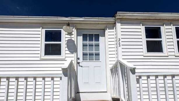 A two-story building with a white exterior, a front door, and a small set of steps leading to the entrance. - Cozy Coastal Cottage Right on the Water’s Edge in North Truro, Massachusetts (North Truro)