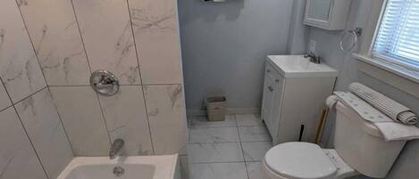 A bathroom with a bathtub, toilet, and sink, marble tiles, and a towel rack.