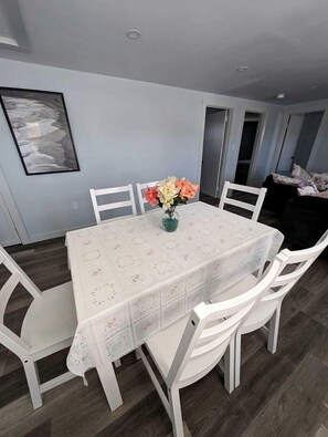 Un comedor con una mesa dispuesta para cuatro personas, sillas blancas y un jarrón con flores.