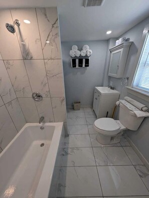 Un baño con bañera, inodoro y lavamanos, azulejos de mármol y un perchero para toallas.