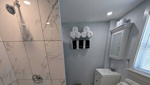 A bathroom with a bathtub, toilet, and sink, marble tiles, and a towel rack. - Cozy Coastal Cottage Right on the Water’s Edge in North Truro, Massachusetts (North Truro)