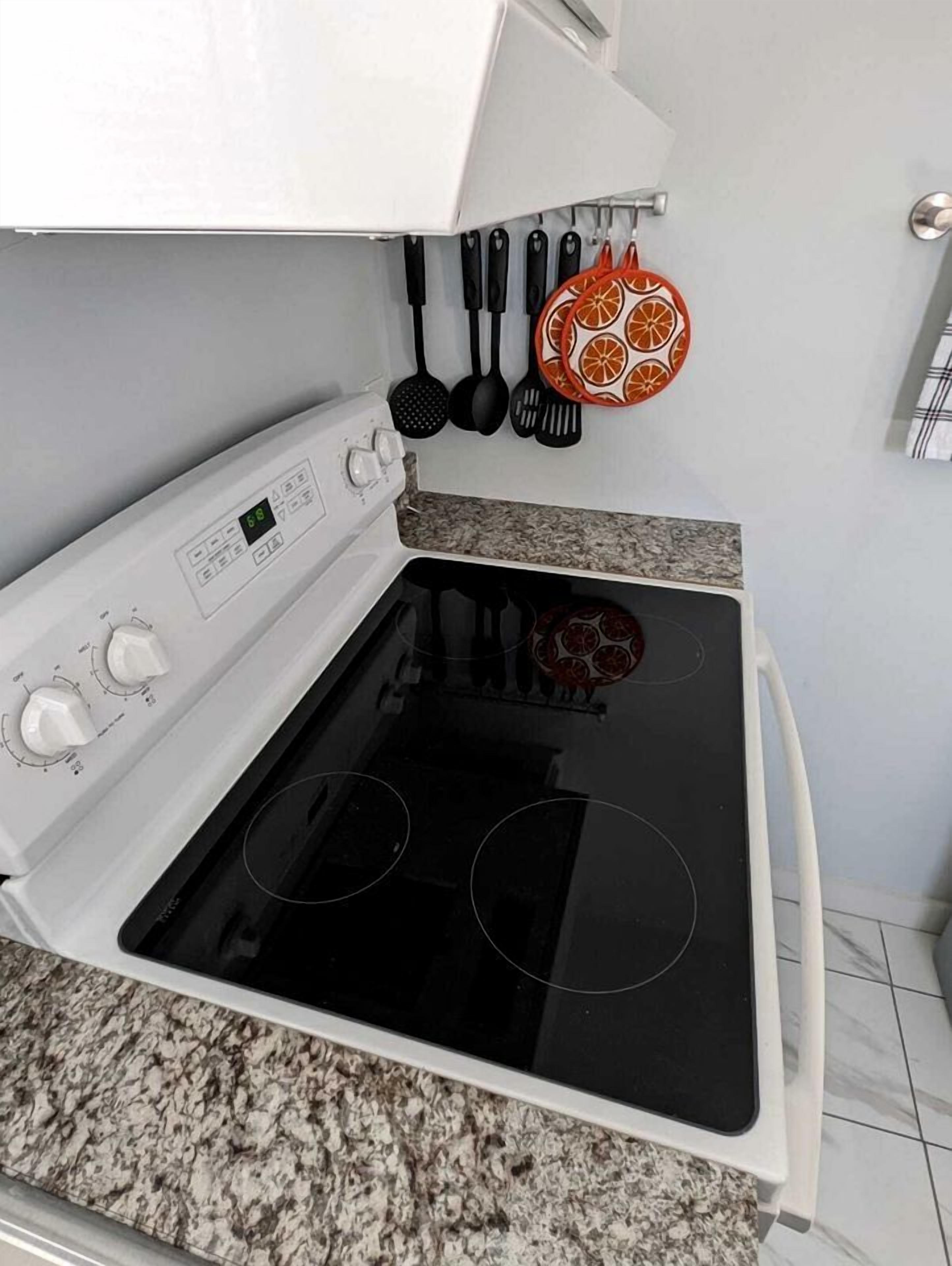 A kitchen with a white stove, granite countertop, and a hanging rack with kitchen utensils.