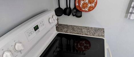 A kitchen with a white stove, granite countertop, and a hanging rack with kitchen utensils.