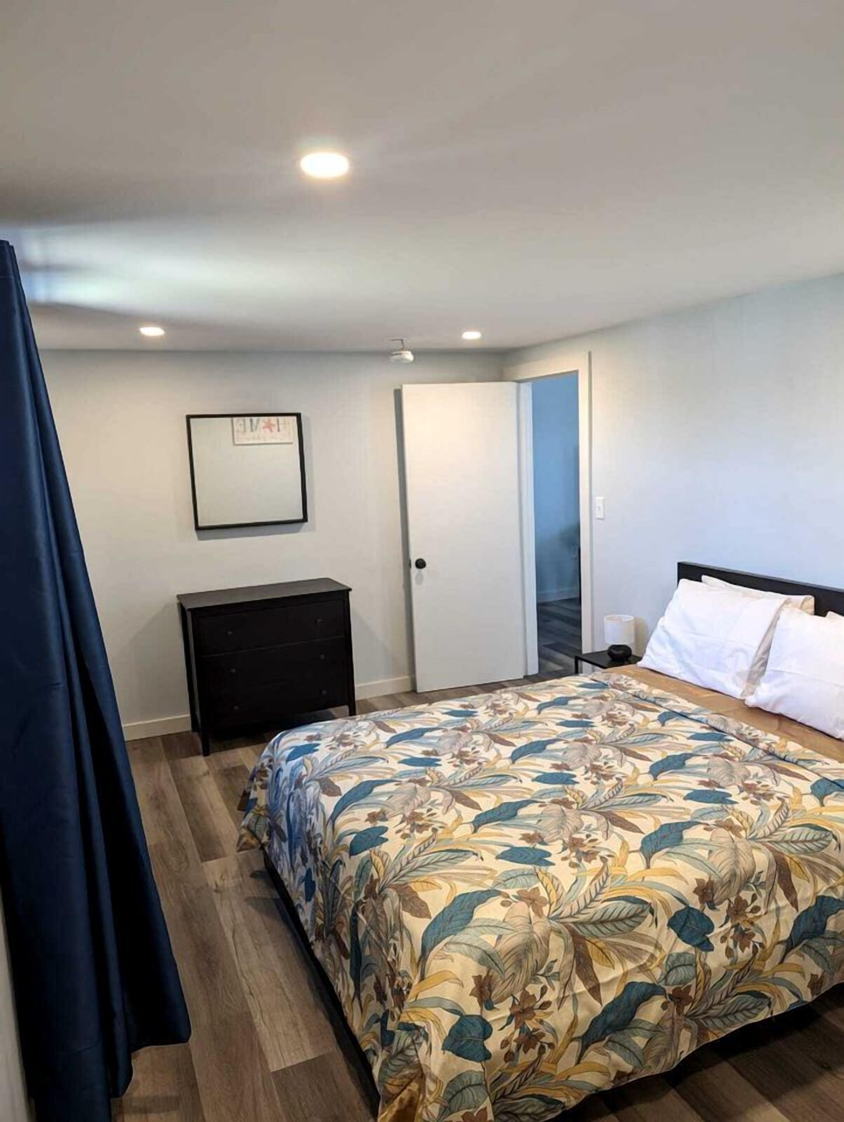 A bedroom with a bed, a dresser, a door, and a framed picture on the wall.