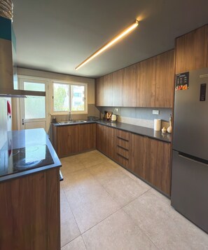 Een moderne keuken met houten kastjes, een roestvrijstalen koelkast en een raam dat natuurlijk licht binnenlaat.