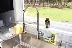 A kitchen sink with a modern faucet, a dish rack, a yellow sponge, a soap dispenser, and a vase on the windowsill.