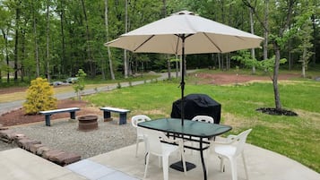 Eine Terrasse im Freien mit Tisch, Stühlen, einem großen Sonnenschirm und einem Grill.