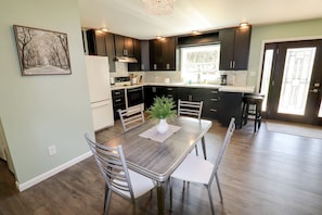 A modern kitchen with dark cabinets, a white refrigerator, and a dining table with chairs.
