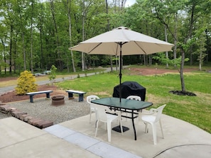Un patio al aire libre con una mesa, sillas, un paraguas grande y una parrilla.