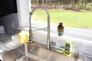 Un lavabo de cocina con un grifo moderno, un escurreplatos, una esponja amarilla, un dispensador de jabón y un florero en el alféizar de la ventana.