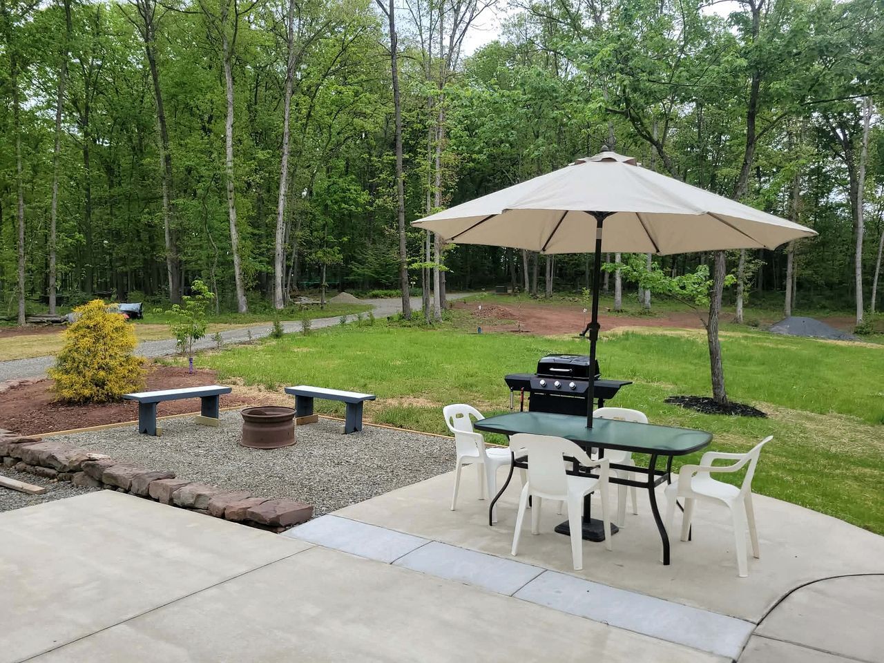 Eine Terrasse im Freien mit Grill, Tisch, Stühlen und einem großen Sonnenschirm.