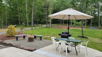 Eine Terrasse im Freien mit Grill, Tisch, Stühlen und einem großen Sonnenschirm.